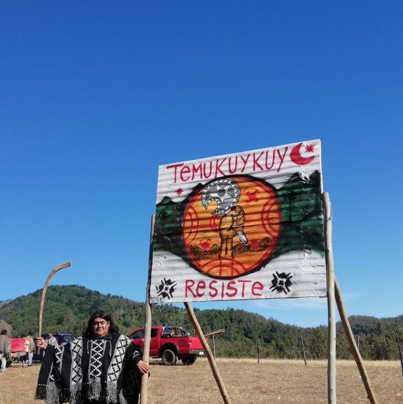 Jorge Huenchullán in traditioneller Kleidung vor einem Schild: "Temucuicui resiste". (Temucuicui leistet Widerstand)